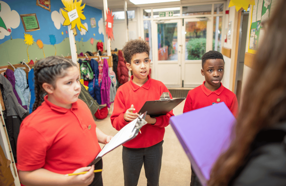 Three students stood with clipboards, talking to a teacher.