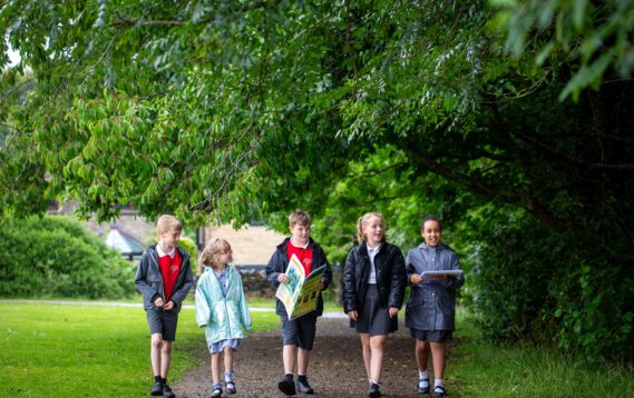 A group of five students walking through some woodland.
