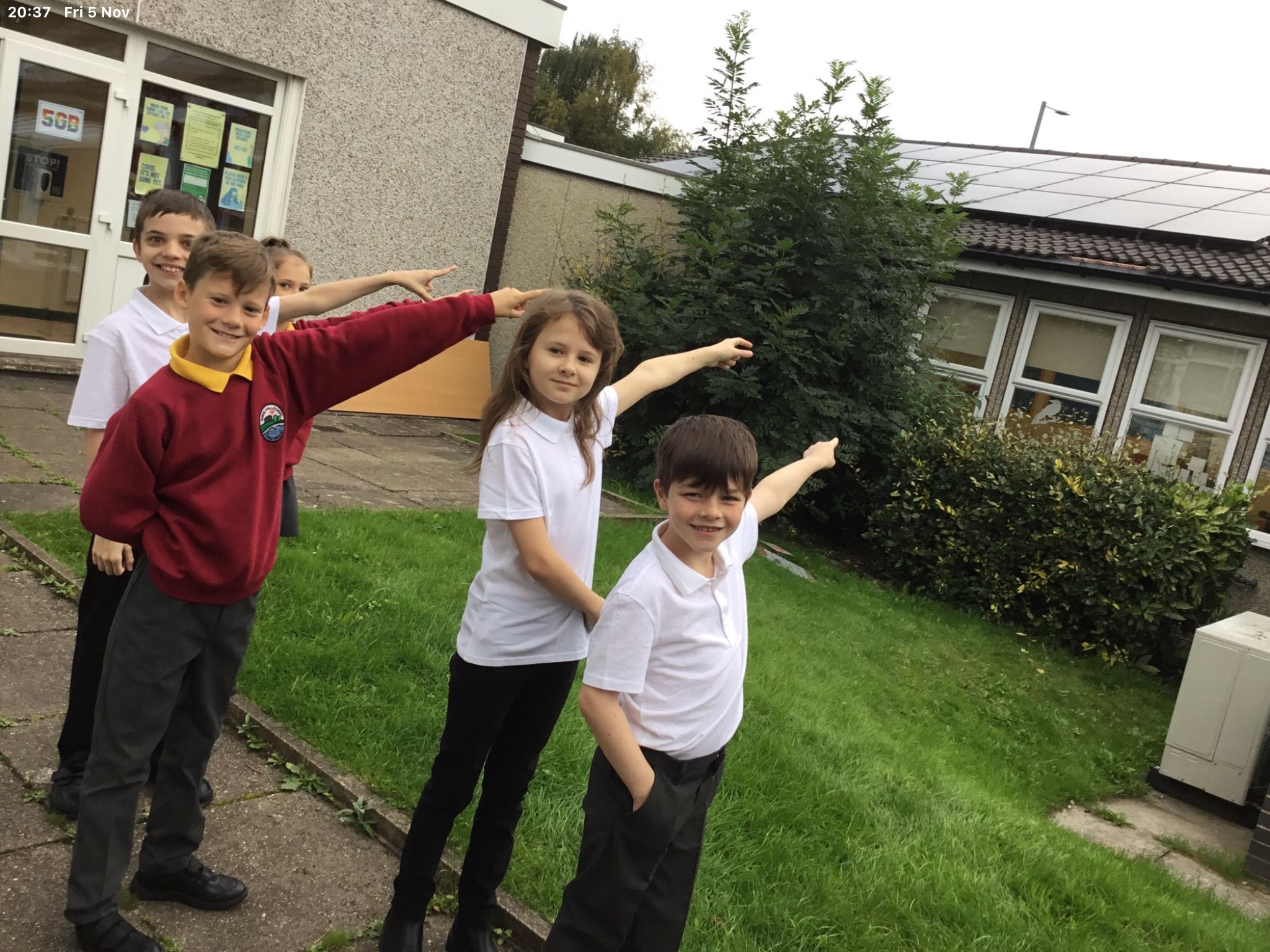A group of three young students pointing at solar panels on their school roof.